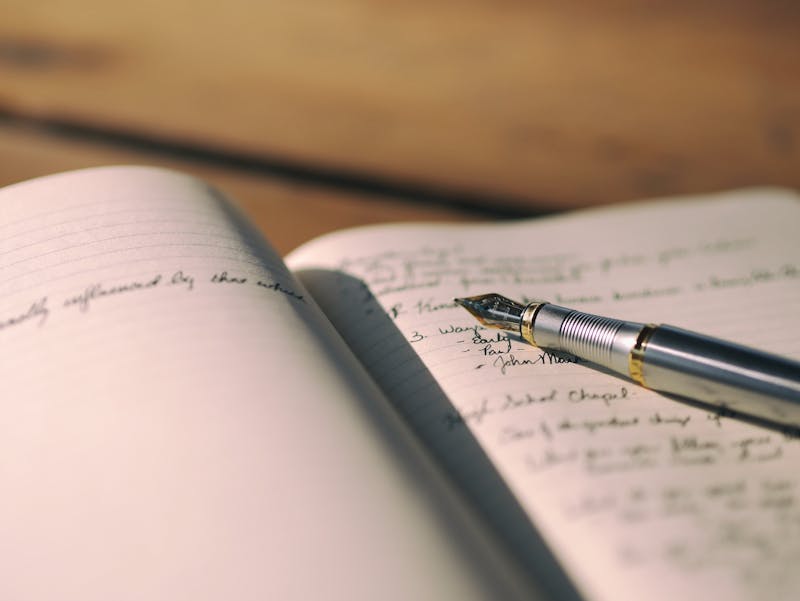 A pen laying on a book. The book is open and there is writing on the pages.