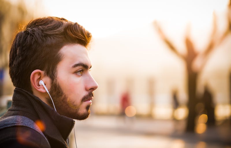 A guy with ear phones in sitting looking to the right.