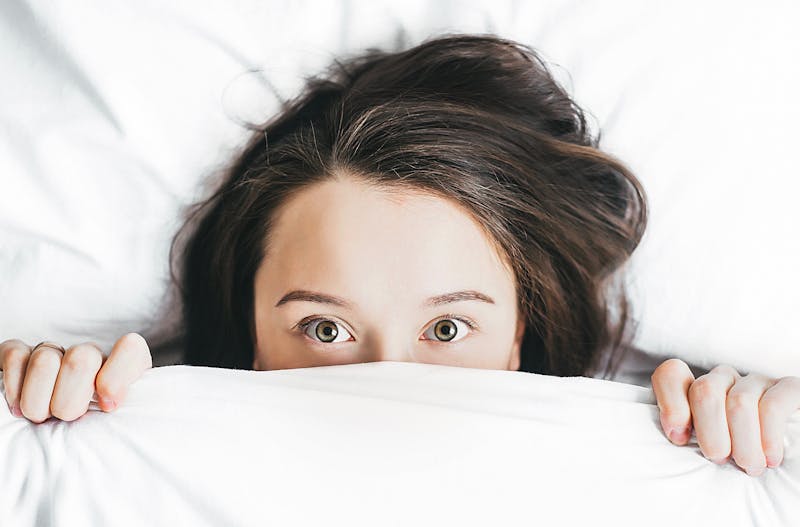 a girl sticking her head out of the white sheet.  just her head from her eyes up and hands are visible