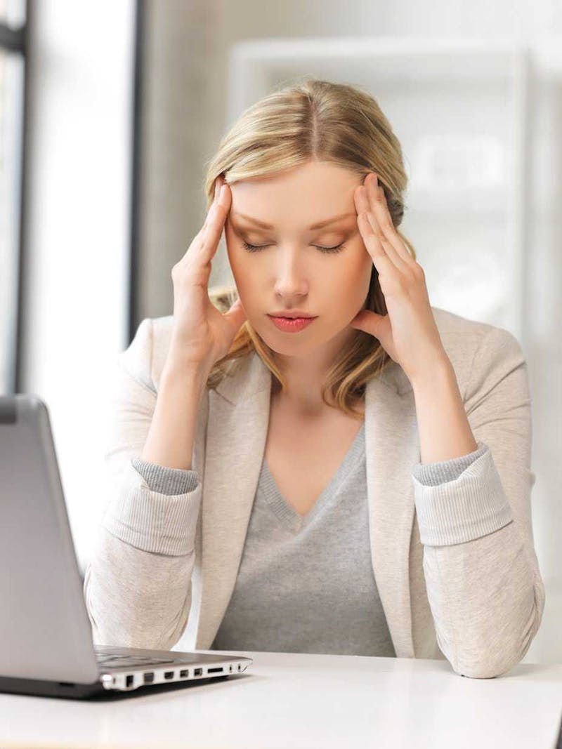 Woman sitting at desk with head in hands.