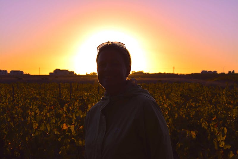 Anita in a vineyard with the sunset behind her.