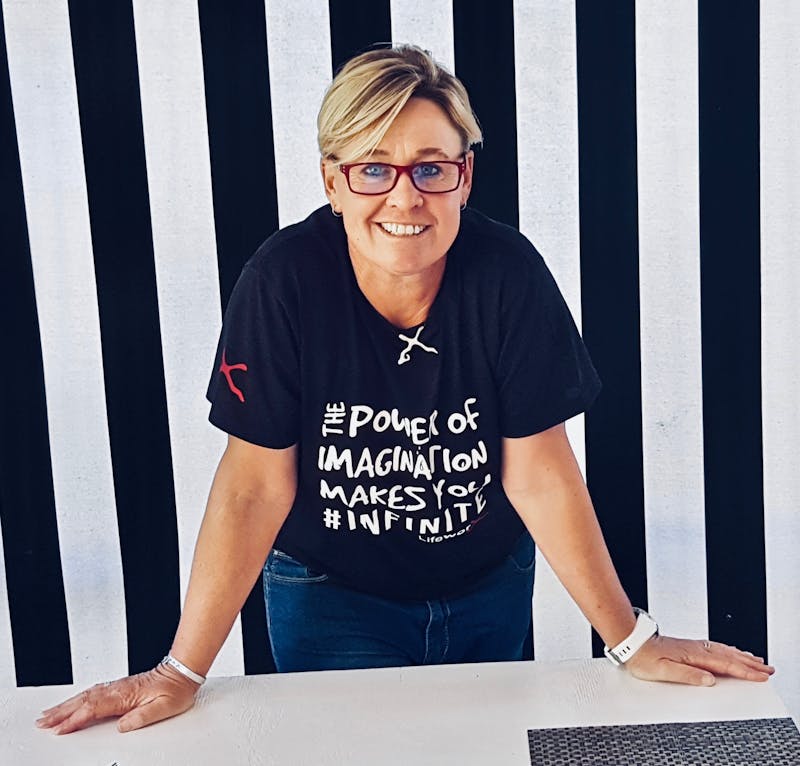 Anita leaning on a table wearing a LifeworX shirt in Cape Town. The background is stripey.