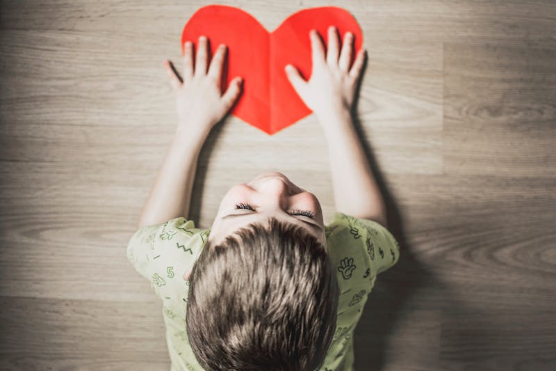 a little boy looking down on a wooden board at a heart