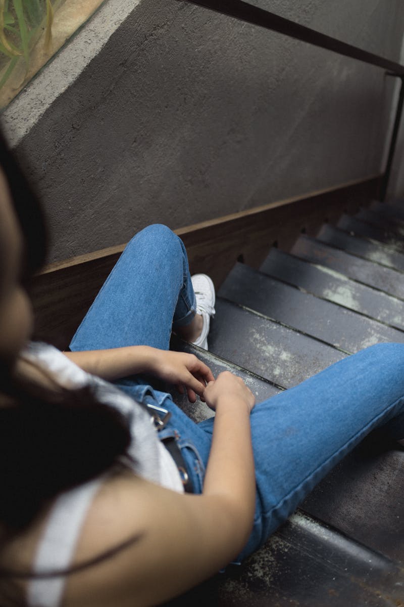 Woman sitting on stair case wearing jeans