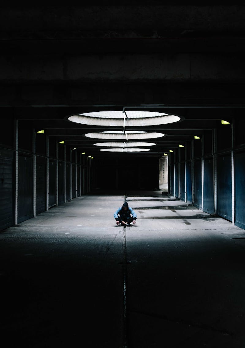 A picture of a boy/man sitting alone in a warehouse