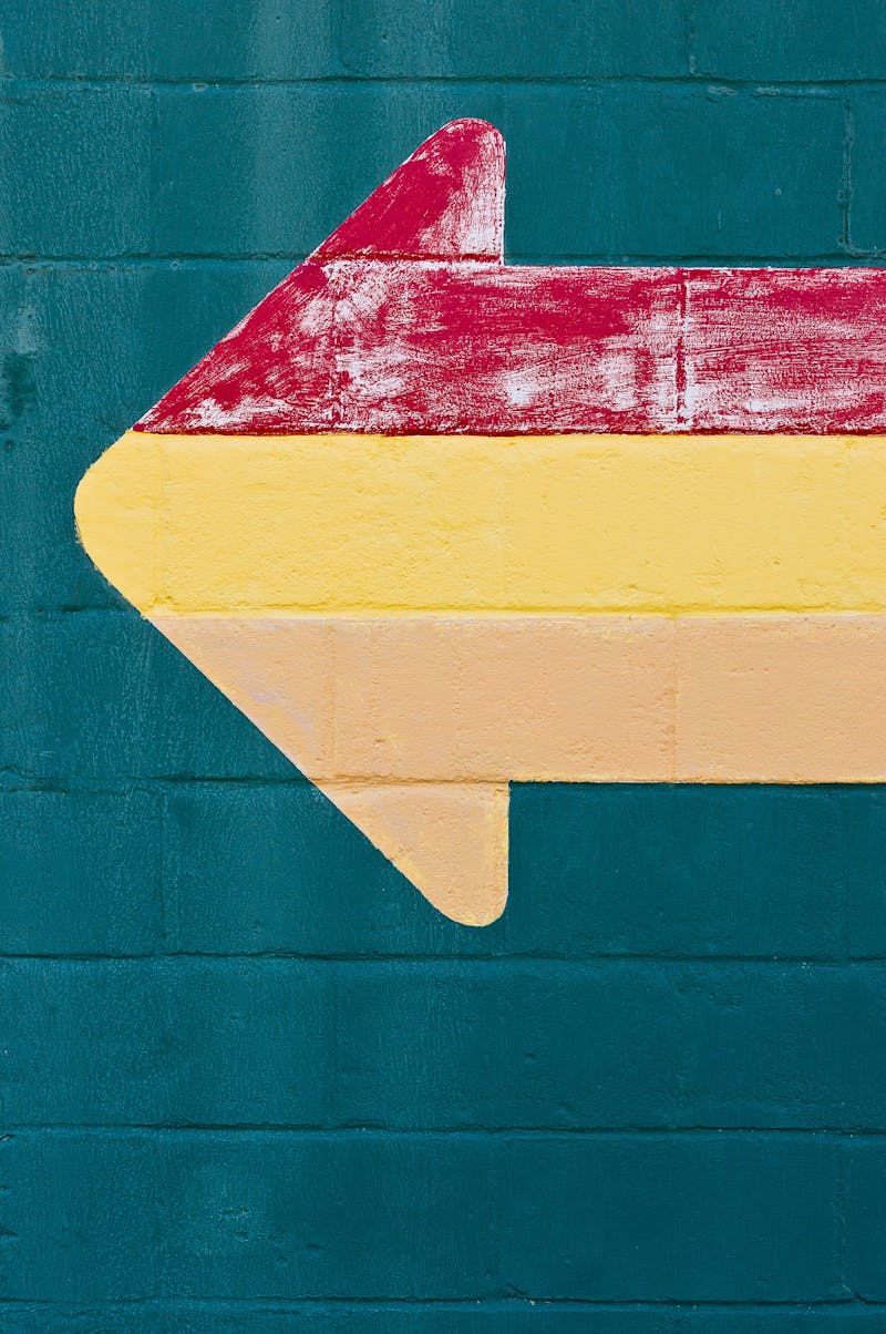 A colourful arrow on a green-painted wall. The arrow is a mixture of red, green and a kind of orange-white.