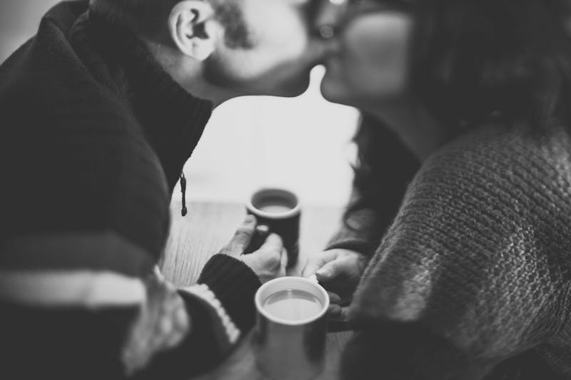 A couple kissing over coffee in black and white photo.