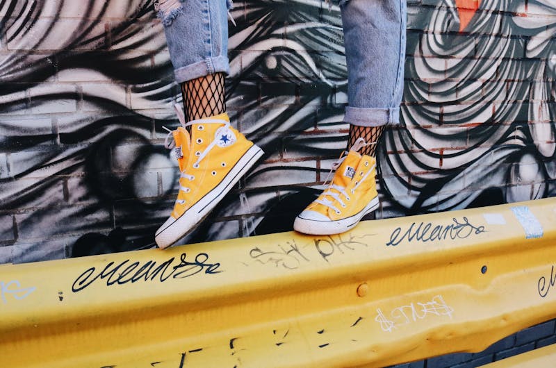 someone with yellow tackies on balancing on a metal structure with graffiti on the wall