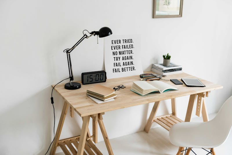 A desk with some books on it and a tablet. There is a paper visible with a quote written on it.