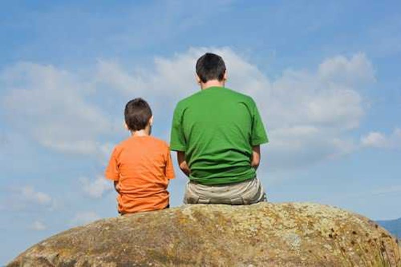 Father sitting next to his son on a rock.