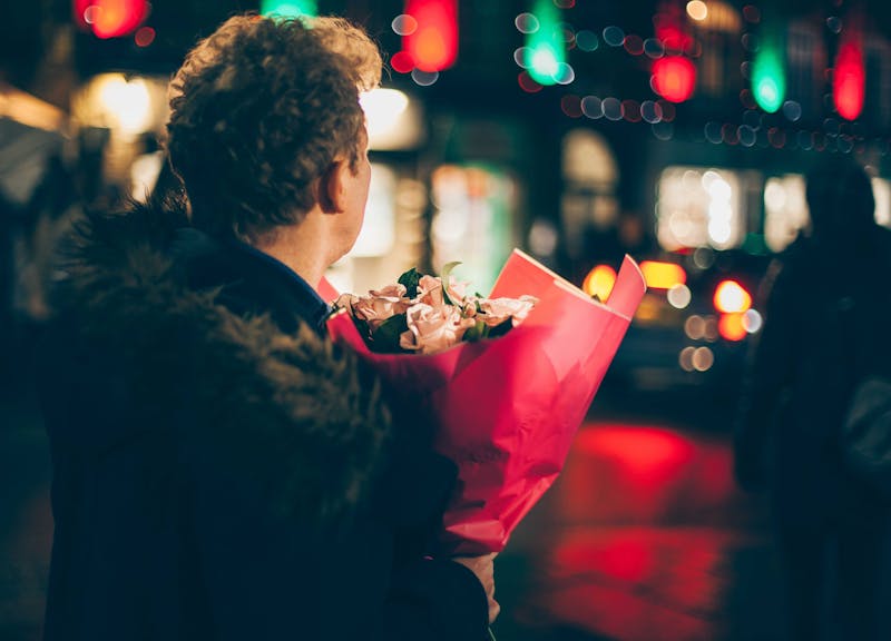 A guy holding a bunch of flowers facing a street.