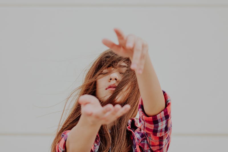 A blond girl wearing a red shirt with her hand stretched out towards the camera letting go of something in the wind.