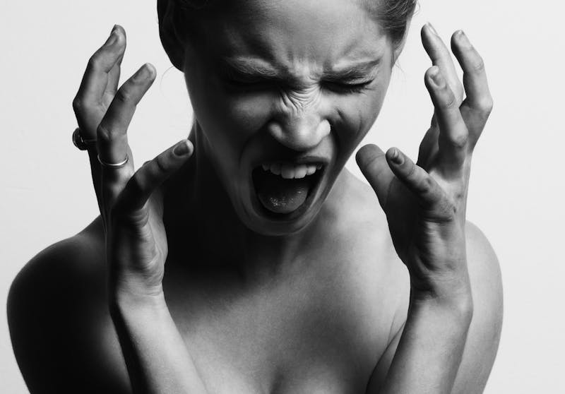 A black and white picture of a woman with no shirt on and hands up as she screams