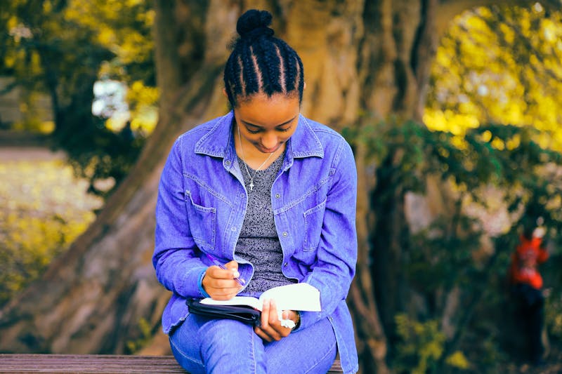 A woman sitting on a bench with her head hanging down writing a list