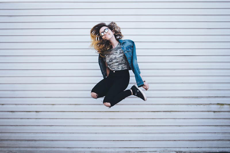 A girl jumping wearing sunglasses and a denim jacket.