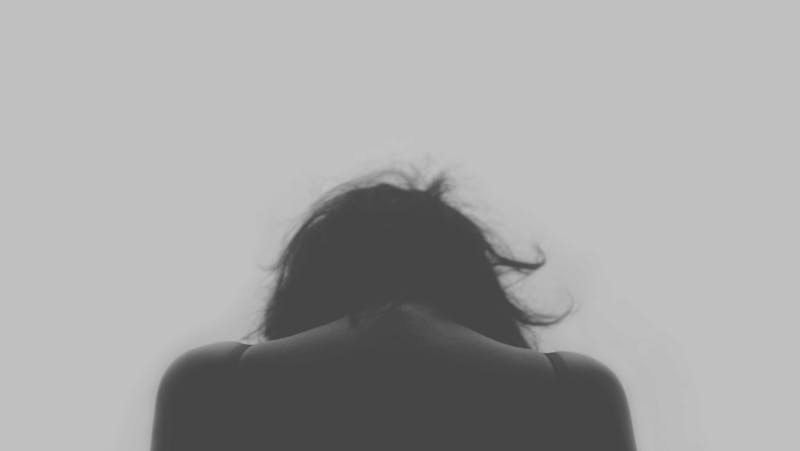 A girl with her head down facing away from the camera. A photo without much colour.
