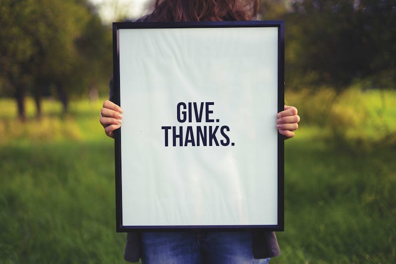 The text, "Give Thanks", printed on a canvas held up by a woman.