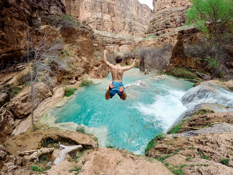 A guy jumping in a river from a cliff. The picture was taken from behind while he is still in mid-air.