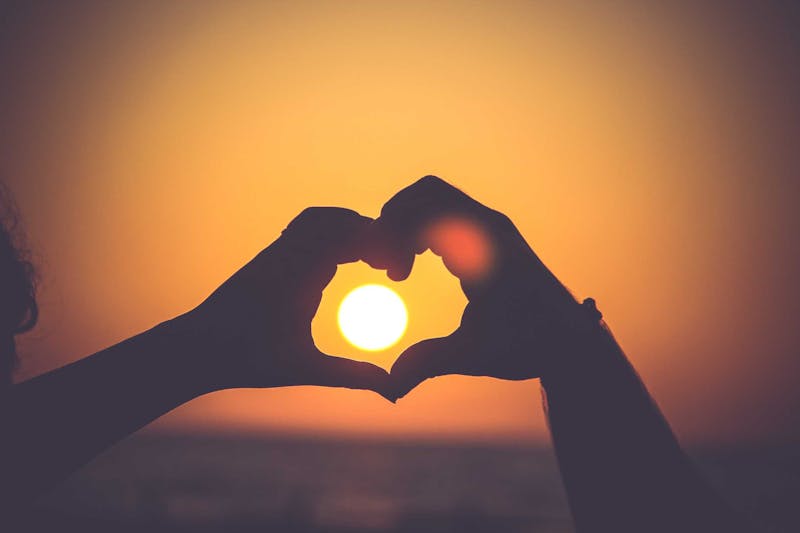 Hand making a heart with the sunset in the background