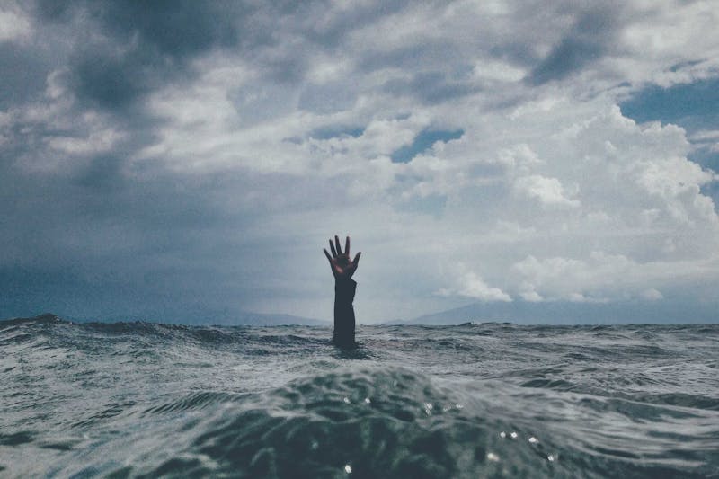 A person's visible hand reaching out from under the ocean's waters.