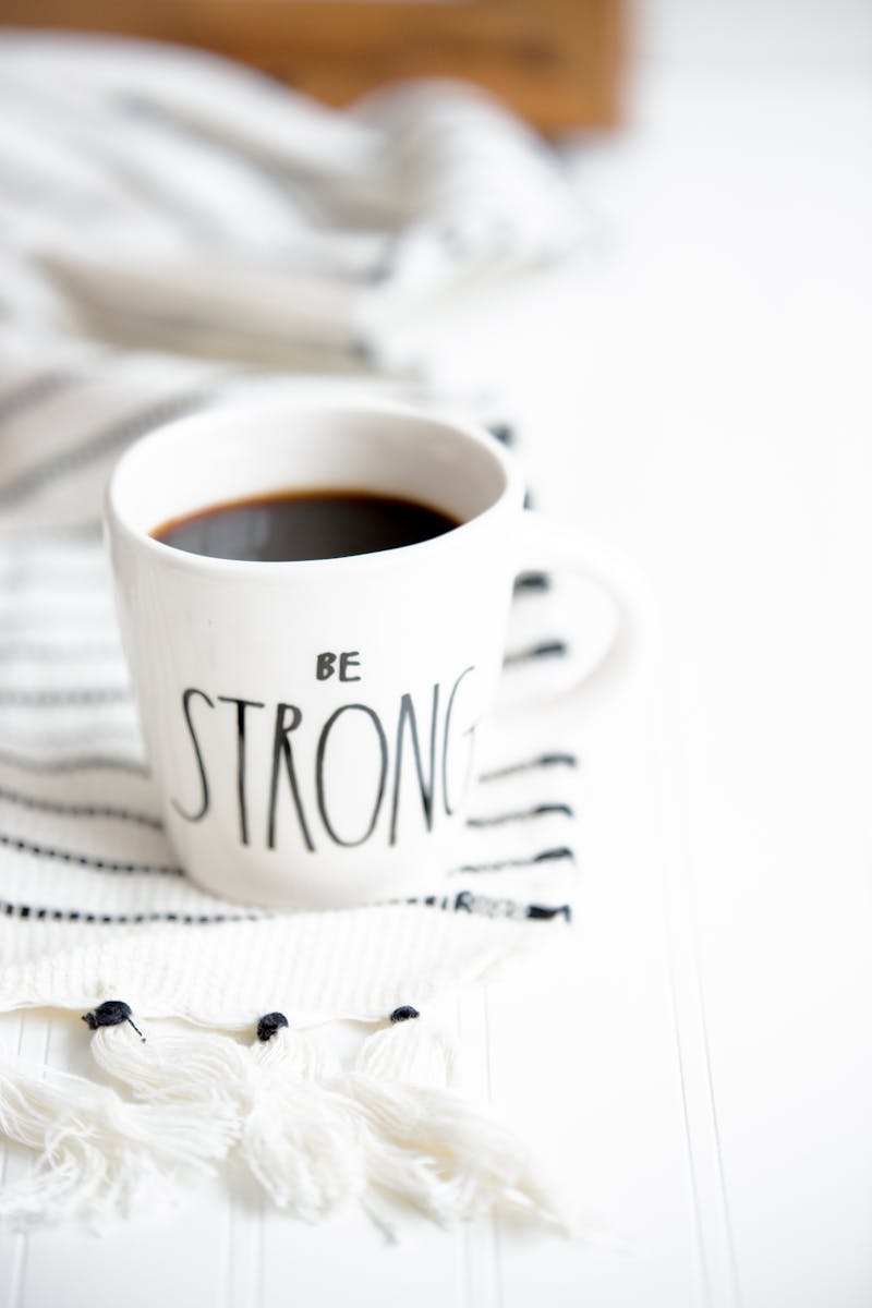 a coffee mug on a white sheet with a saying on it saying Be Stong