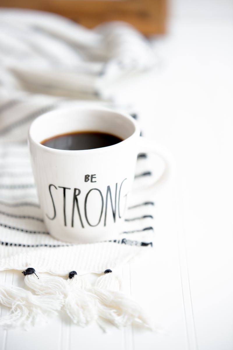 a  coffee mug on a white sheet with a saying on it saying Be Stong