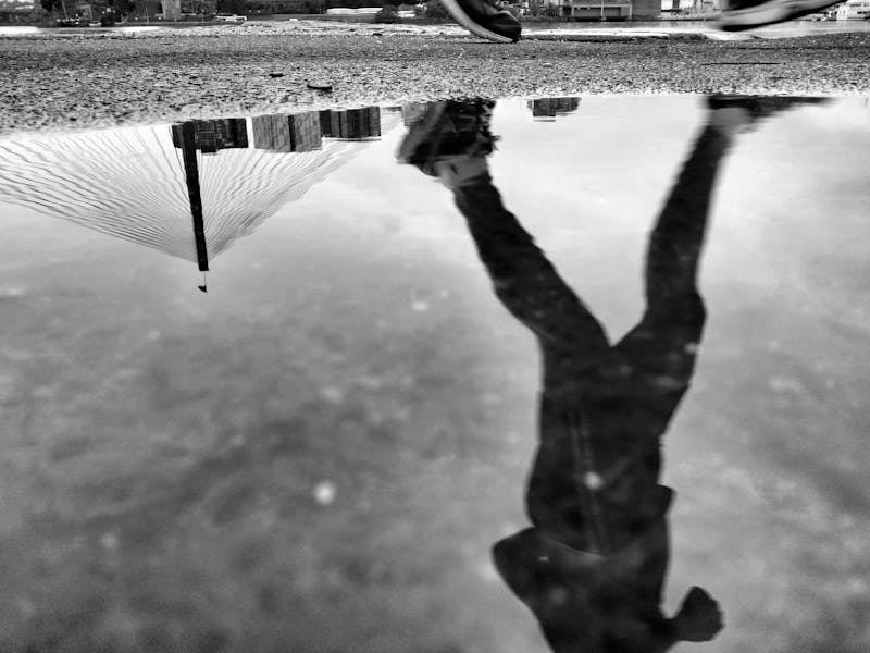 A black and white picture of a man running with his reflecting in the water