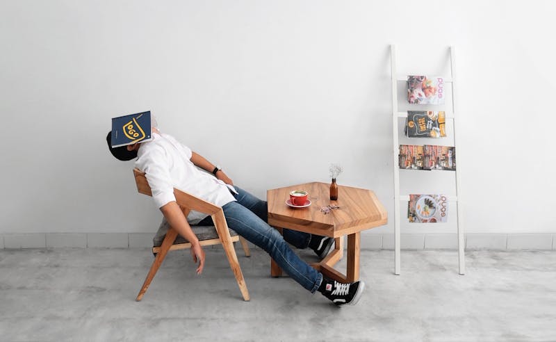 A man sitting in a chair stretched out with a book covering his face