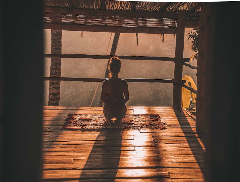 A young woman sitting meditating with her back to us in a wooden cabin