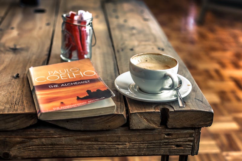 a Poaulo Coelho book the Alchemist on a coffee talbe alongside a cup of coffee