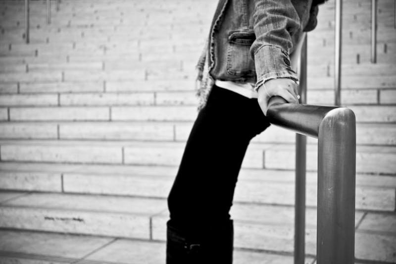 a black and white picture of a girl/boy leaning up against a railing wearing a denim jacket. you can only see the torso