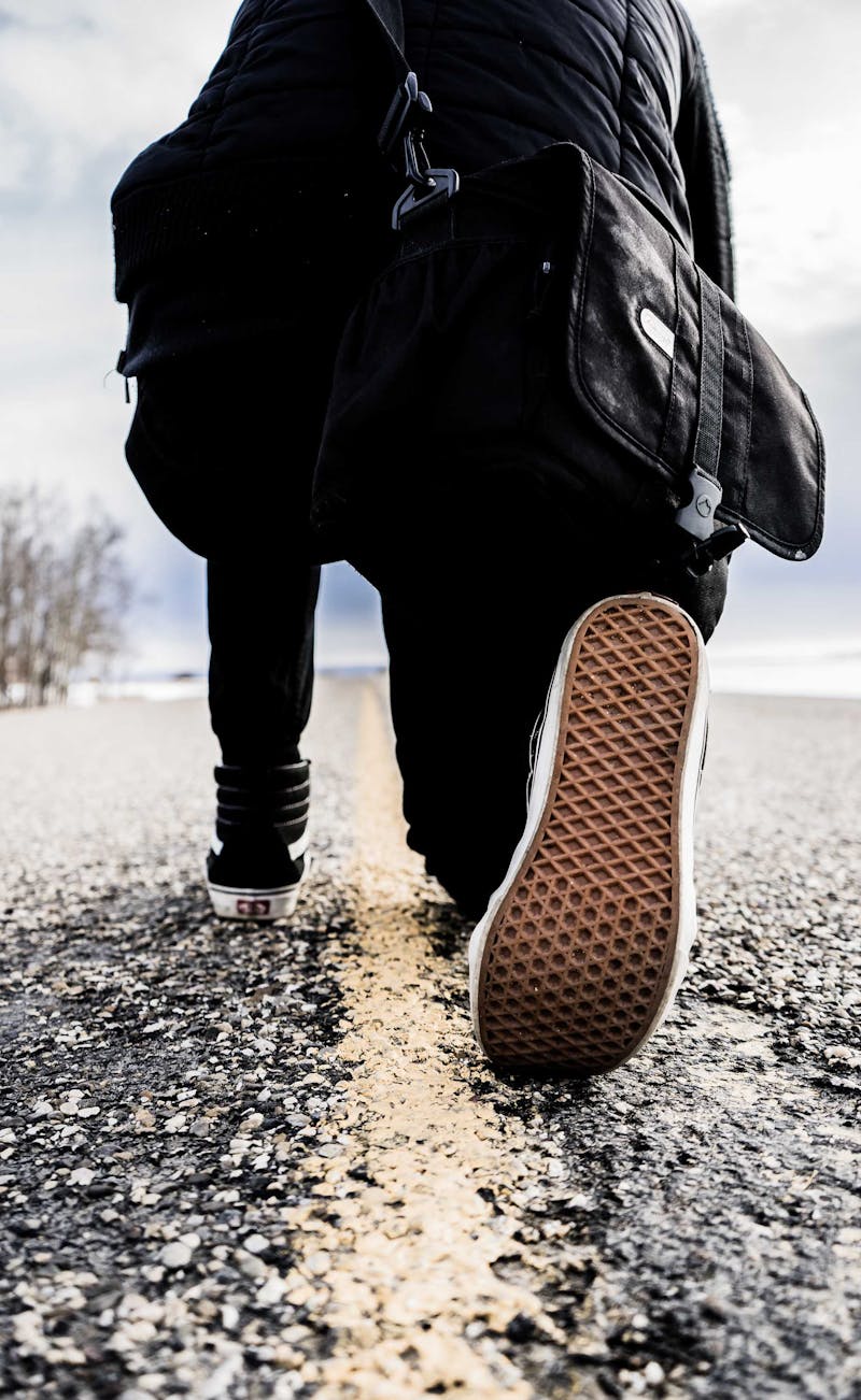 Person kneeling in road carrying a satchel.