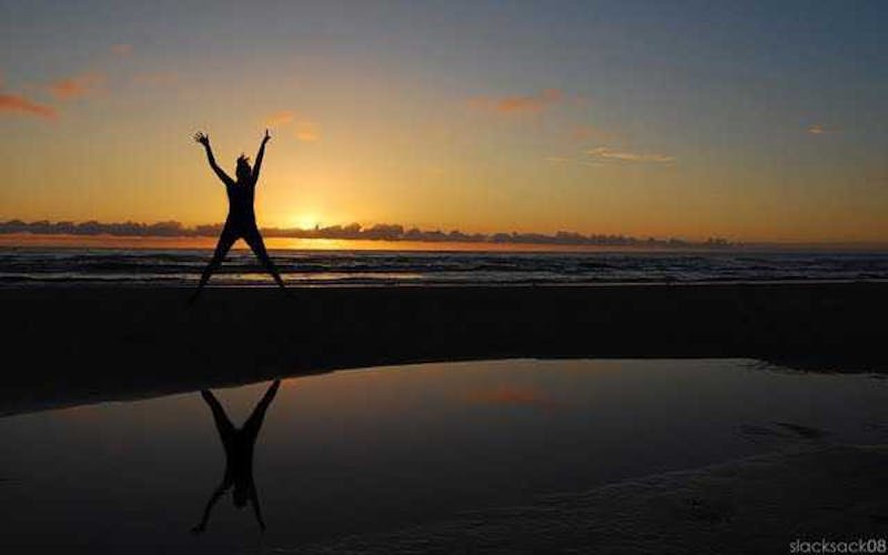Woman jumping in X shape on beach with sunset in background.