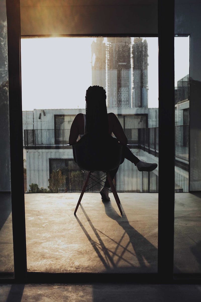 Woman looking out from balcony; sitting.