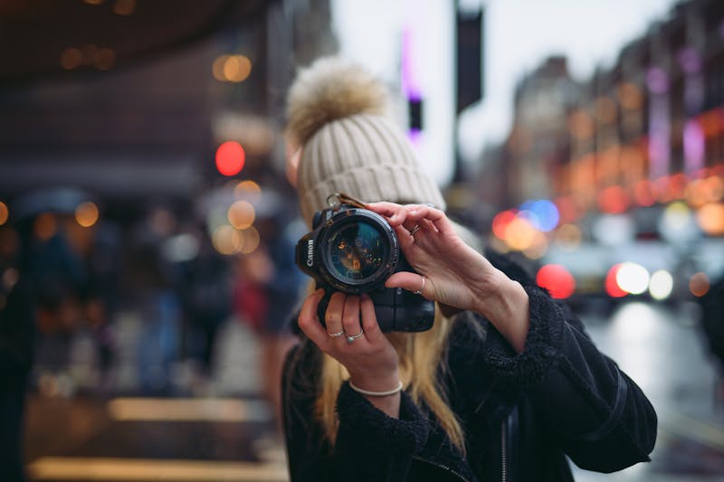 A girl behind a camera with a woolen hat on looking through a camera