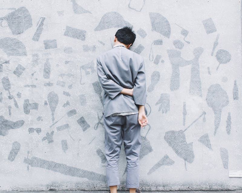 a woman standing right up close to a wall with writing and pictures all over it. She is wearing grey