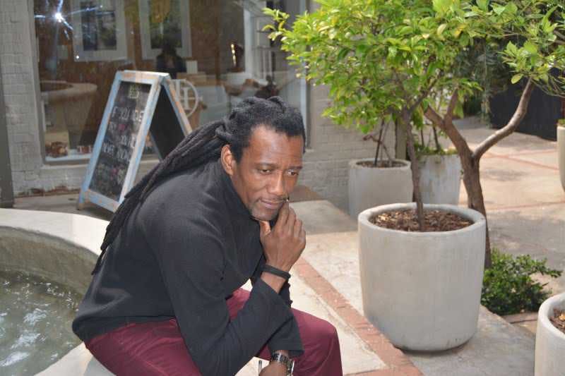 Man with dreadlocks sitting at a fountain.