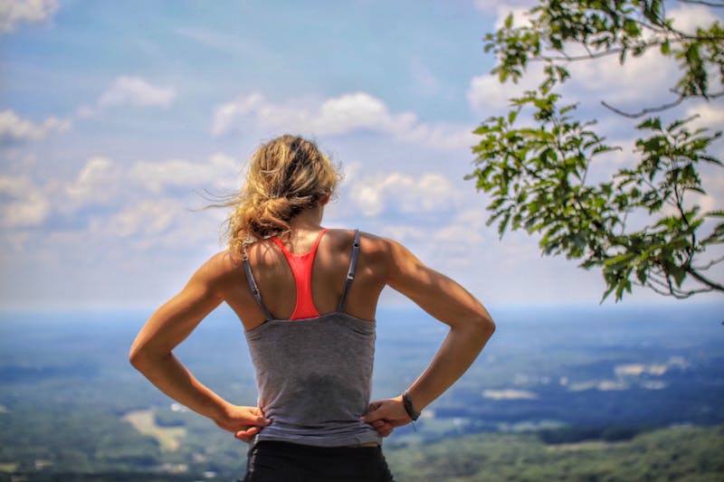 a woman standing with her back to us, with her hands on her hips looking from the top of a hill out at the ocean