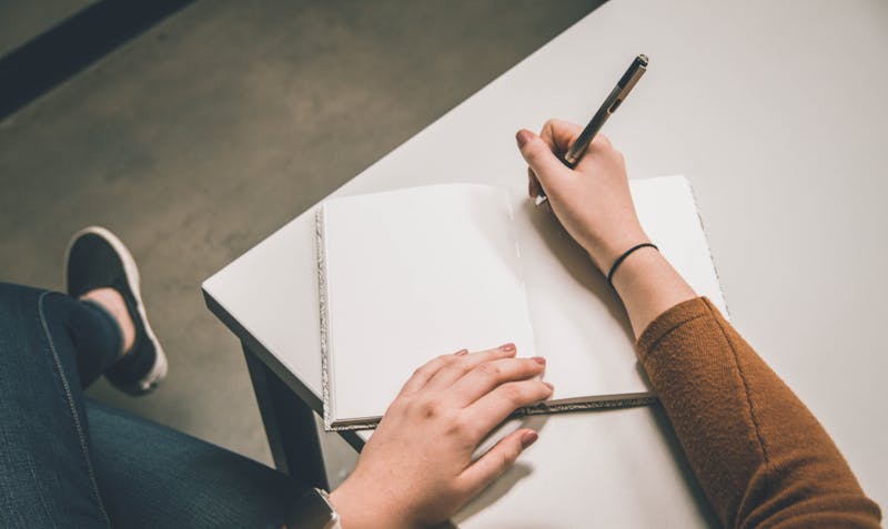 a person sitting at a desk with a note pad and wrting a list