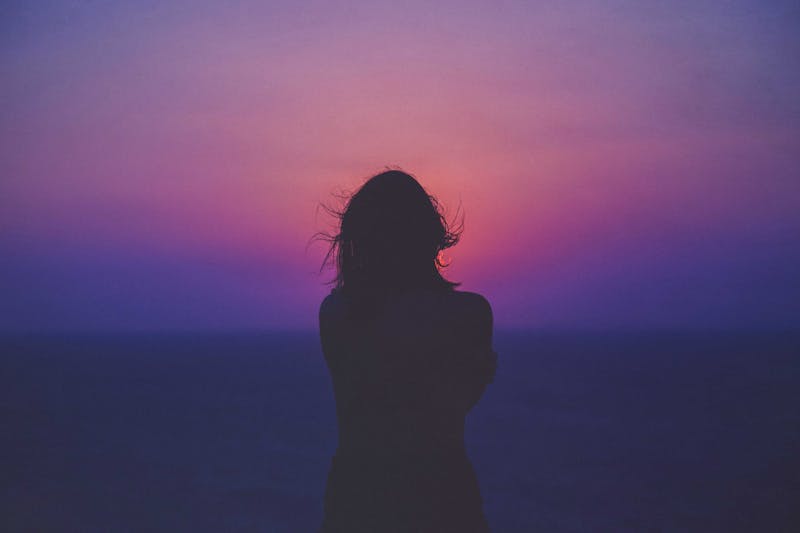 Silhouette of a girl looking into a pink sunset.