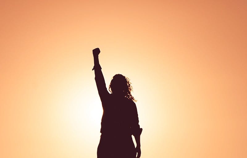 a silhouette of a woman holding up her right arm facing us