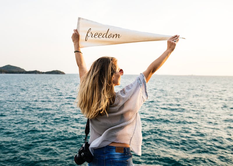 I woman with her back to us looking out at the ocean holding a banner saying freedom