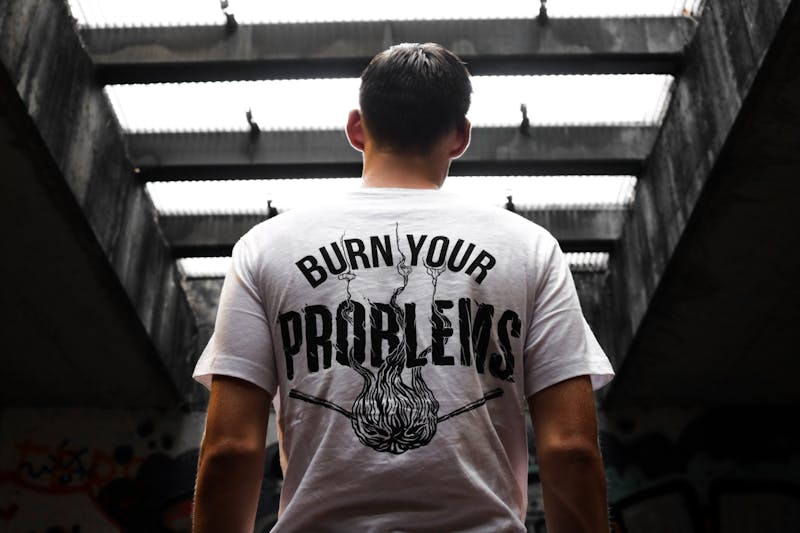 A guy with short hair and his back to us with a white tshirt on saying burn your problems away