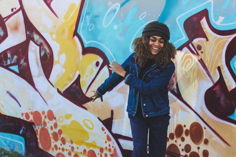 A woman smiling with graffiti painted on the wall in the background.