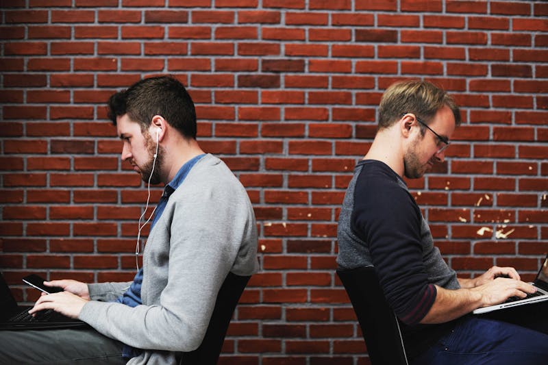 Two men sitting with their backs to one another while working on computers