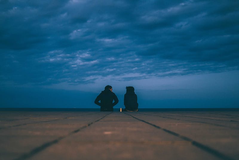 Two people sitting with their backs to us looking out at the ocean and talking