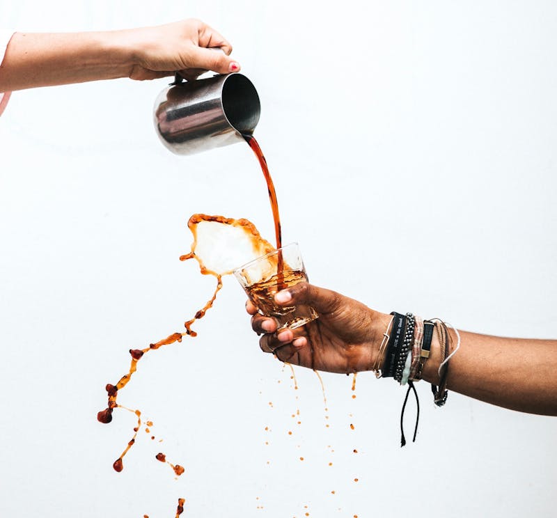 two hands with a white background pour coffee from a jug into a cup