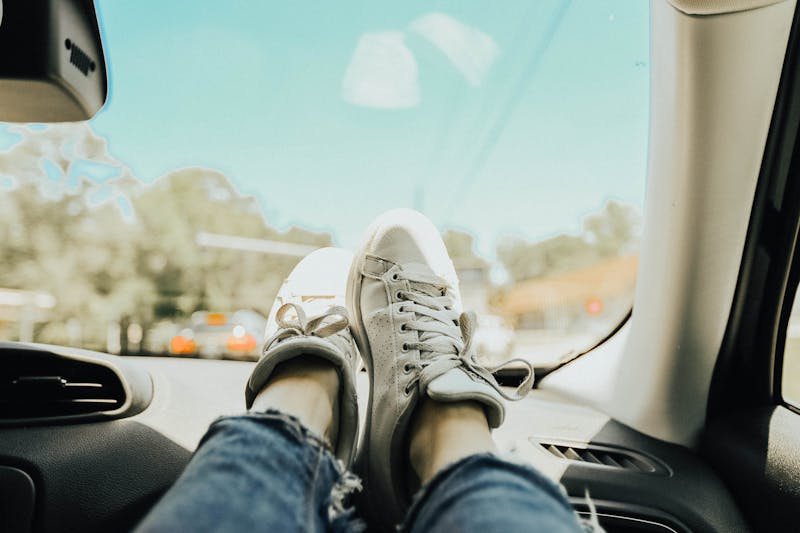 legs crossed with tackies on the dashboard of a car looking our the windscreen of the care