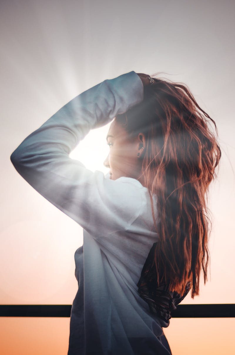 A woman standing with her face to the sun and running her fingers through her hair.
