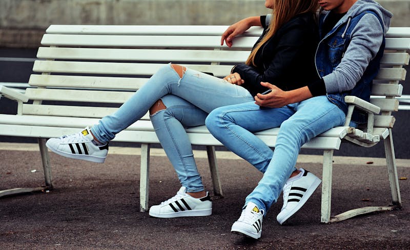 A young couple in jeans sitting on a bench.